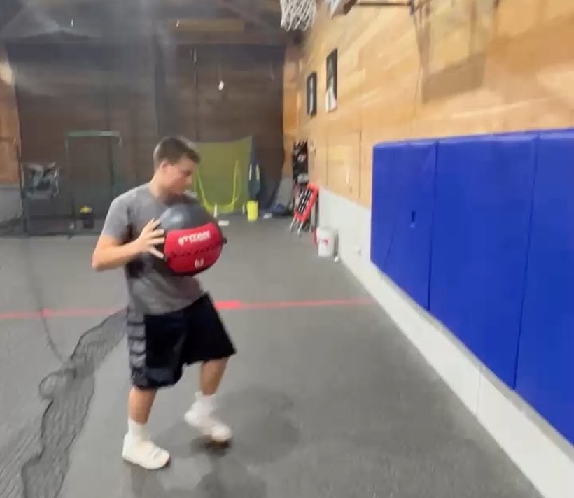 An athlete driving forward with a medicine ball on the court